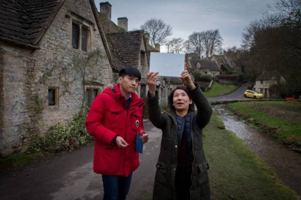 South Korean tourists take a selfie at Arlington Row in Bibury, Cotswolds, where a yellow car has been the cause of controversy for spoiling the view. See SWNS story SWYELLOW; A bright yellow car is photo-bombing England's most picturesque view. Tourists' picture-postcard shot of the Cotswold's Arlington Row are being ruined by "ugly" car - which is appearing in photographs all over the world. The 14th century cottages, owned by the National Trust, are the most photographed cottages in Britain and attract swarms of visitors every year. The car's owner, Peter Maddox, 82, said there was nothing he could do about the banana yellow car.