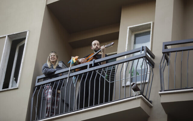 A man plays guitar on the balcony of his home during a flash mob launched throughout Italy to bring people together and try to cope with the emergency of coronavirus, in Milan, Italy, Friday, March 13, 2020. Italians have been experiencing yet further virus-containment restrictions after Premier Giuseppe Conte ordered restaurants, cafes and retail shops closed after imposing a nationwide lockdown on personal movement. For most people, the new coronavirus causes only mild or moderate symptoms. For some it can cause more severe illness. (AP Photo/Luca Bruno)